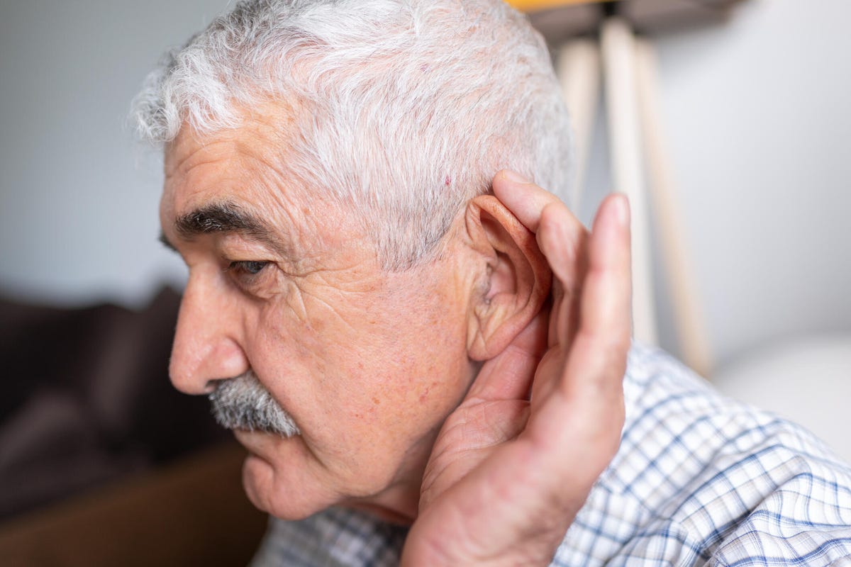 Hombre mayor sosteniendo su aurícula con la mano para oír bien
