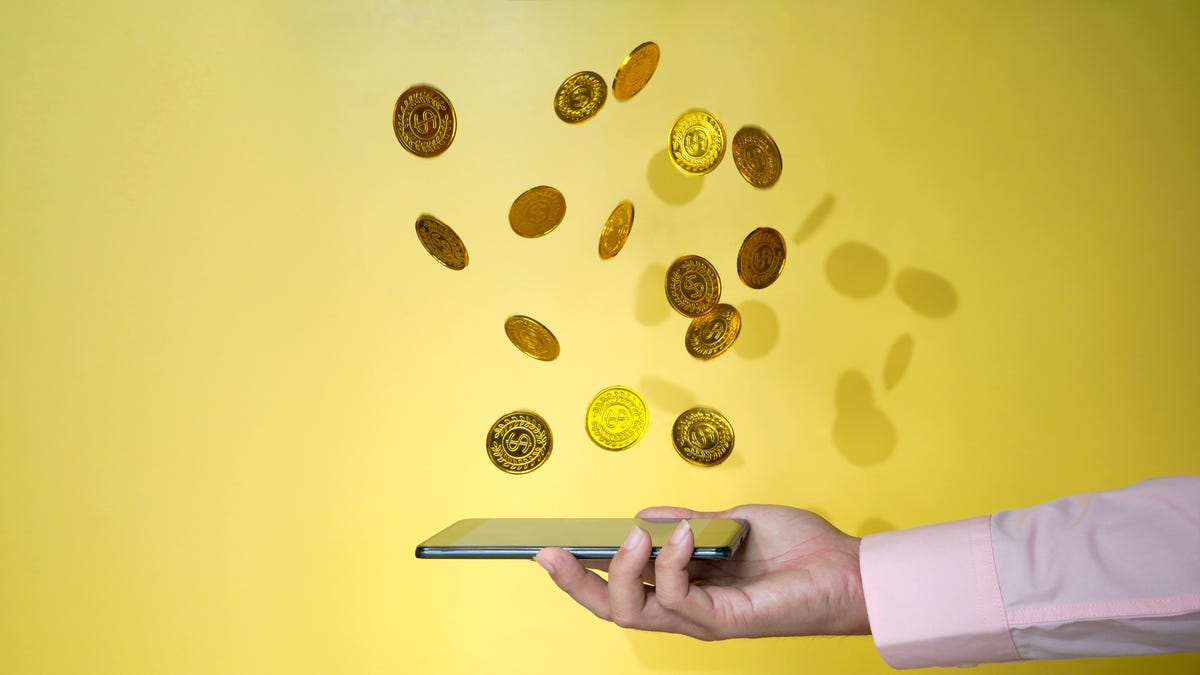Coins above a smart phone in a person's hand.