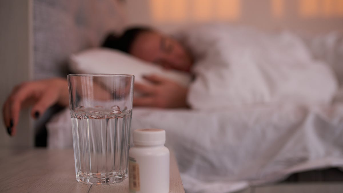 Vitamins and glass of water on a bedside.