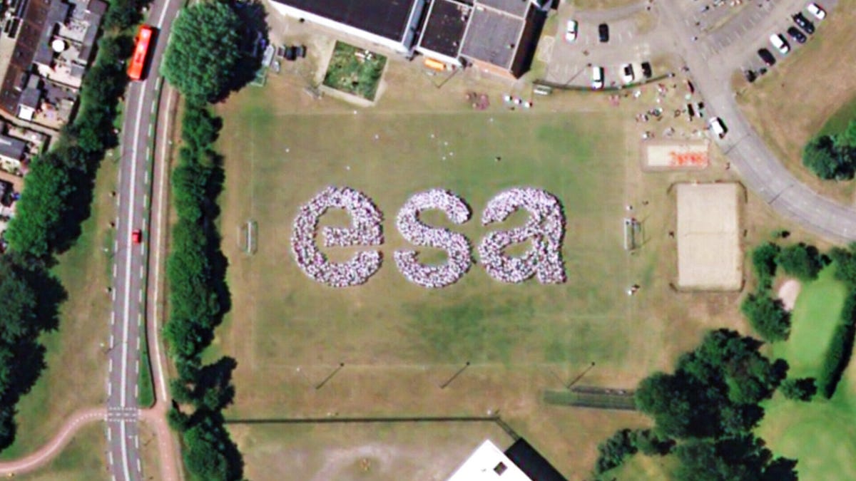 A satellite image shows around 1,000 people grouped together in the letters "ESA" against a green field as seen from an orbiting satellite.