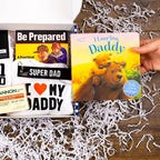 A dad-to-be gift box containing a shirt, socks, soap and books sits on a wooden surface.