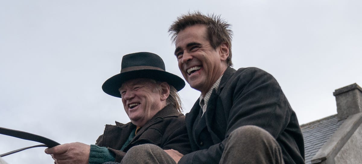 Colin Farrell and Brendan Gleeson laugh while riding a wagon in the movie The Banshees of Inisherin.