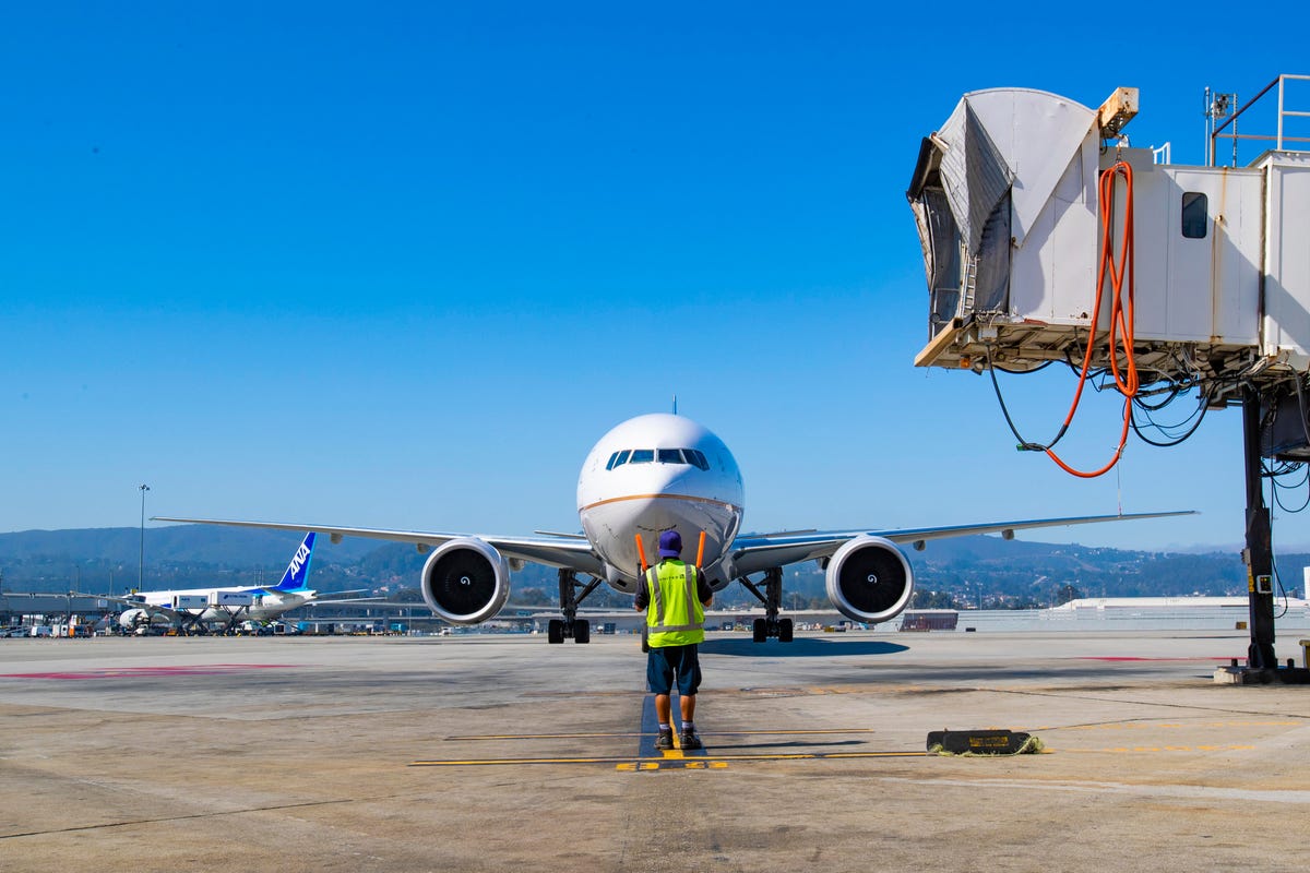 A ground crew member guides a United Airlines Boeing 777 to its gate.