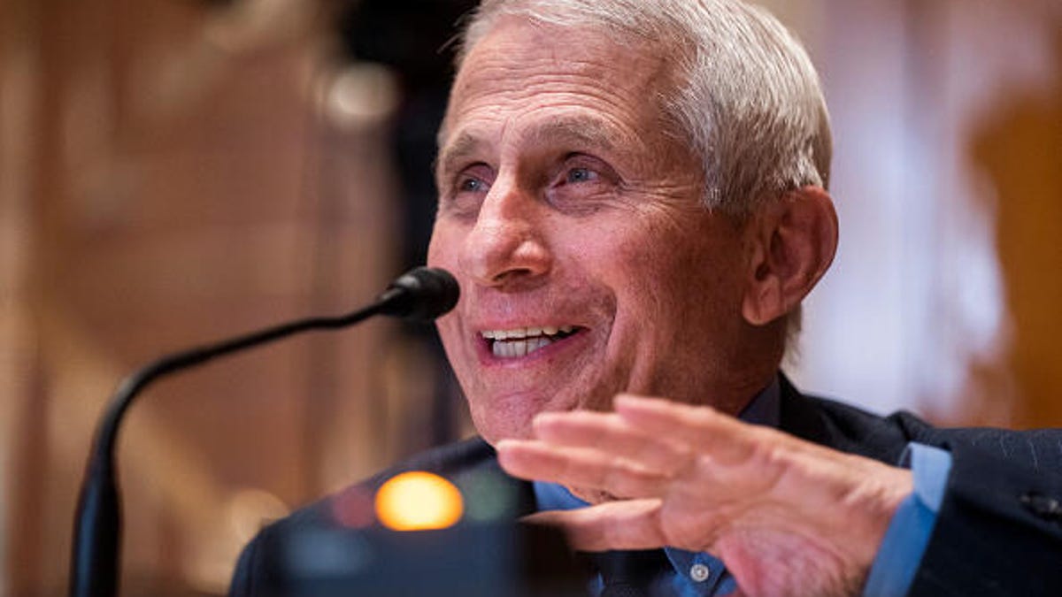 Anthony Fauci speaks at a microphone, gesturing with his left hand