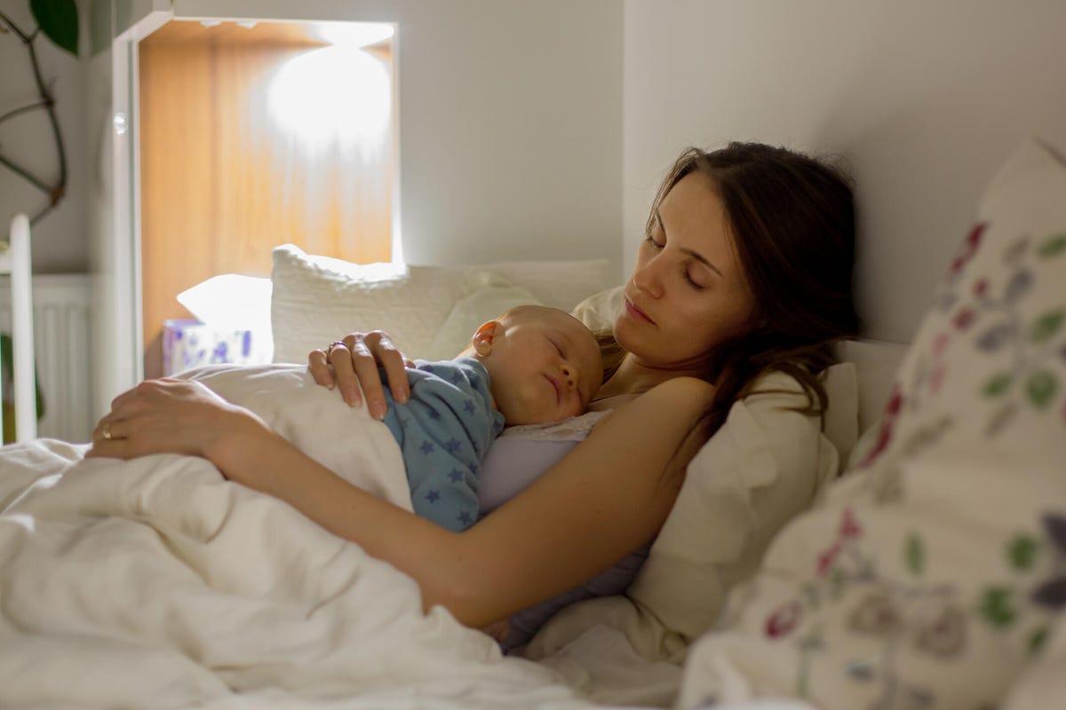 A woman sleeps in bed with her baby on her chest.