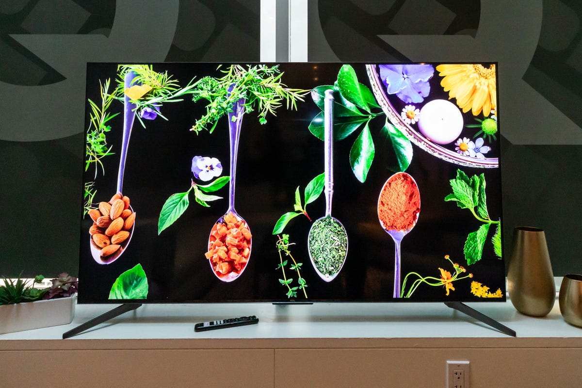 A TCL Q7 TV displaying food next to vases.