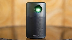 The Anker Nebula Capsule sits on a glass table in front of a blurred background.