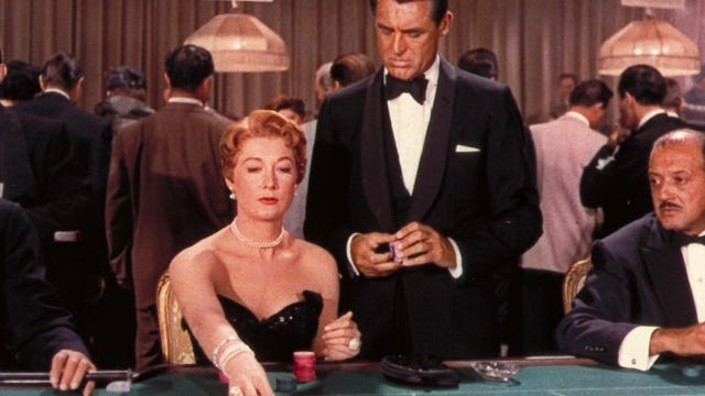 a woman sits at a blackjack table while a man in a tux stands behind her