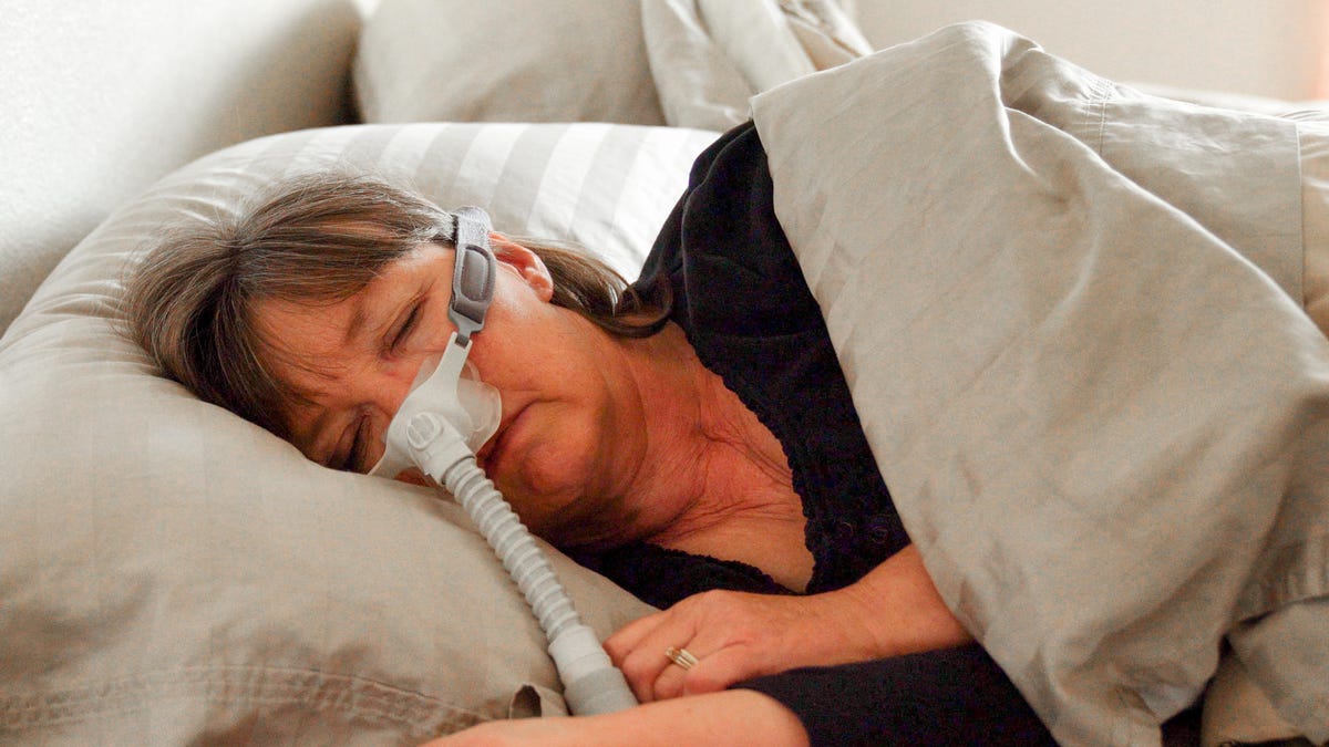 Middle Aged Woman With Sleep Apnea Asleep in a Bed Wearing a CPAP (Continuous positive airway pressure) machine to aid in her sleeping