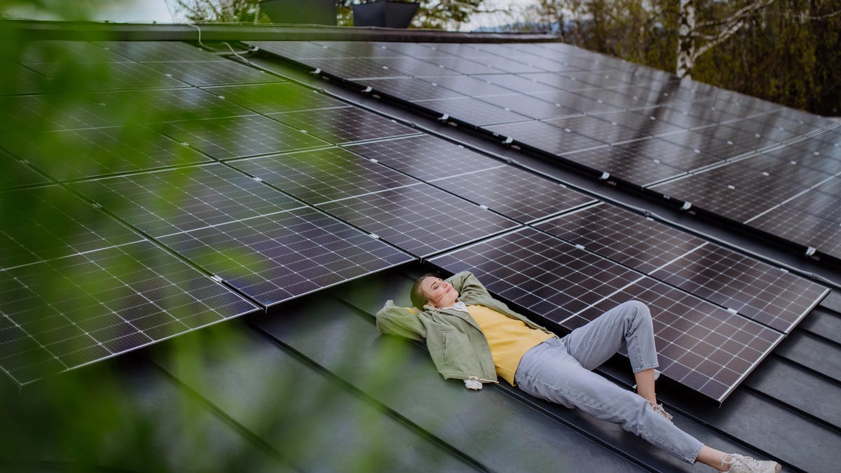 A person laying atop a rooftop filled with solar panels looking satisfied with their decision