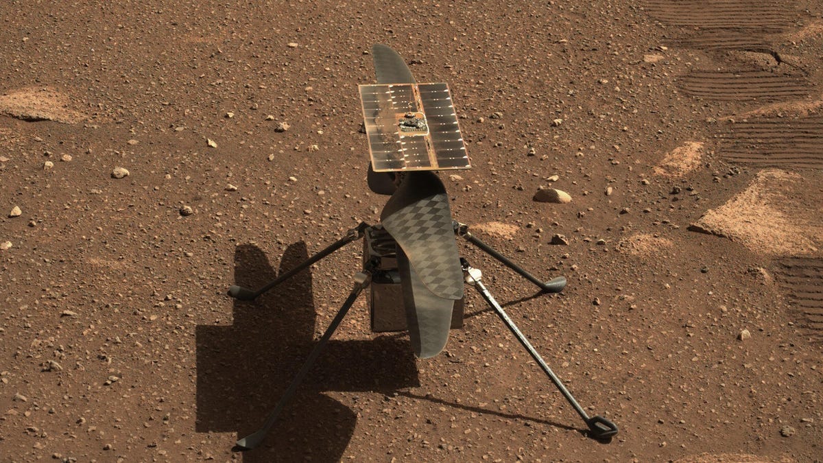 Ingenuity helicopter on Mars, a small solar-paneled rotorcraft on reddish-brown pebbly ground.
