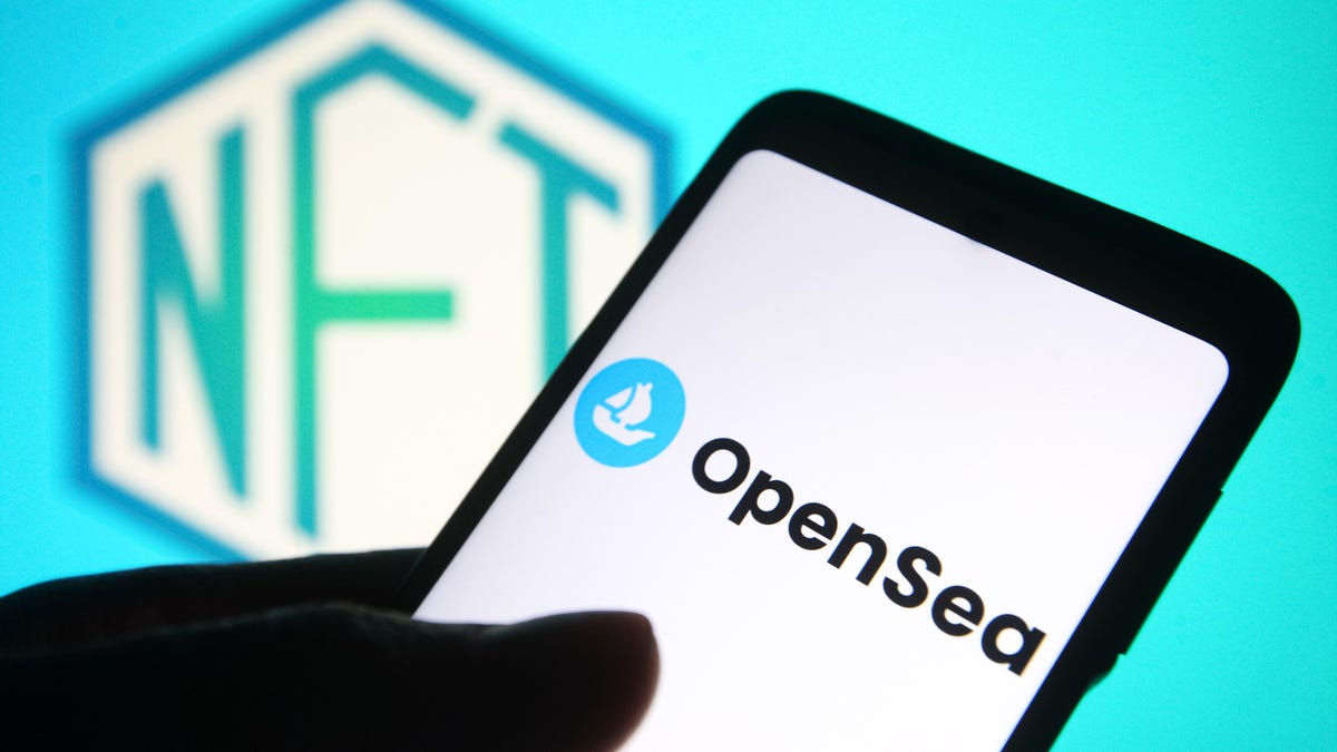 A hand holding a phone with the OpenSea logo displayed, with an NFT logo in the background