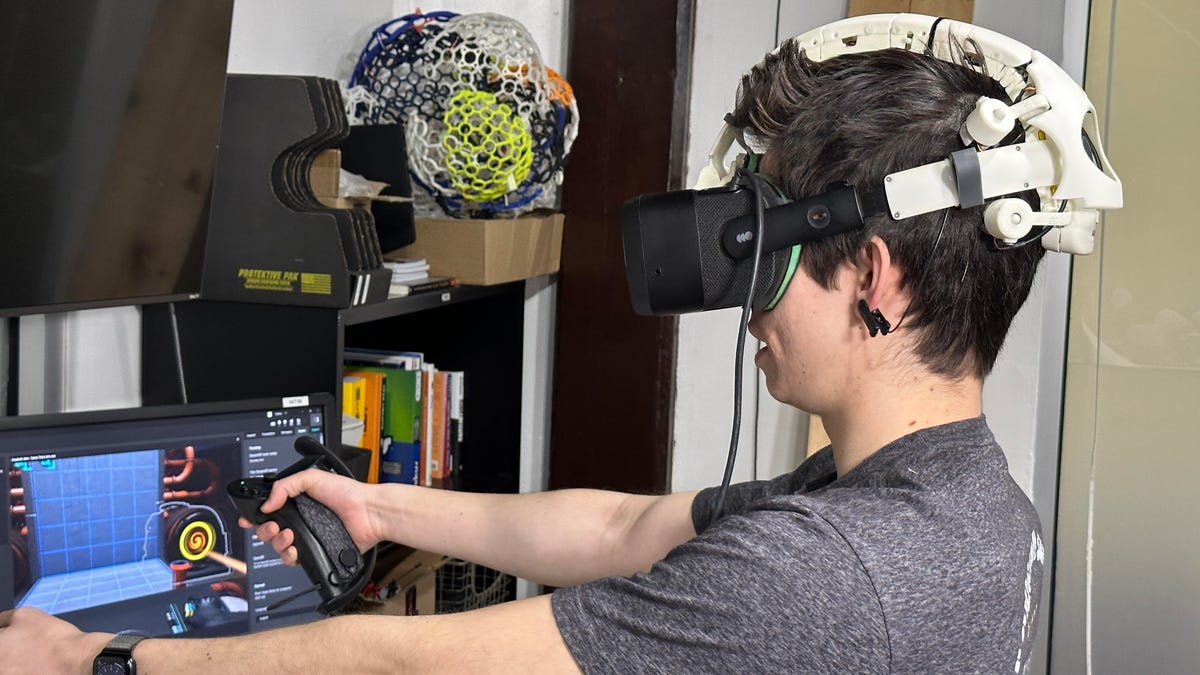 A person wearing a prototype VR headset and holding controllers in front of a desk