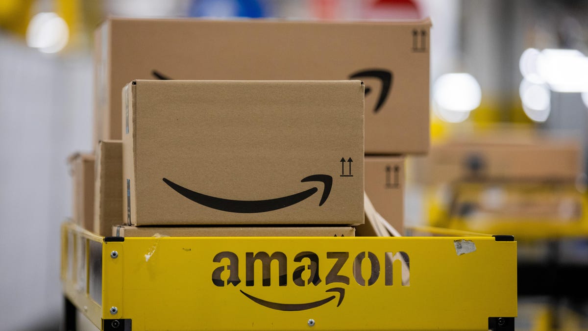 Brown boxes with Amazon&apos;s smiling logo on the side sit on a metal shelf.
