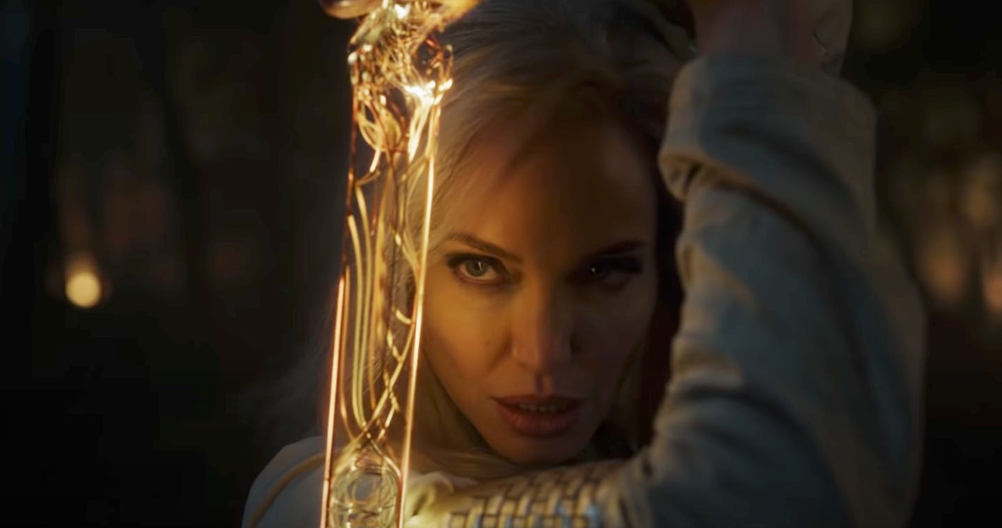 Angelina Jolie's face is illuminated by the glowing gold sword conjured by her superpowers